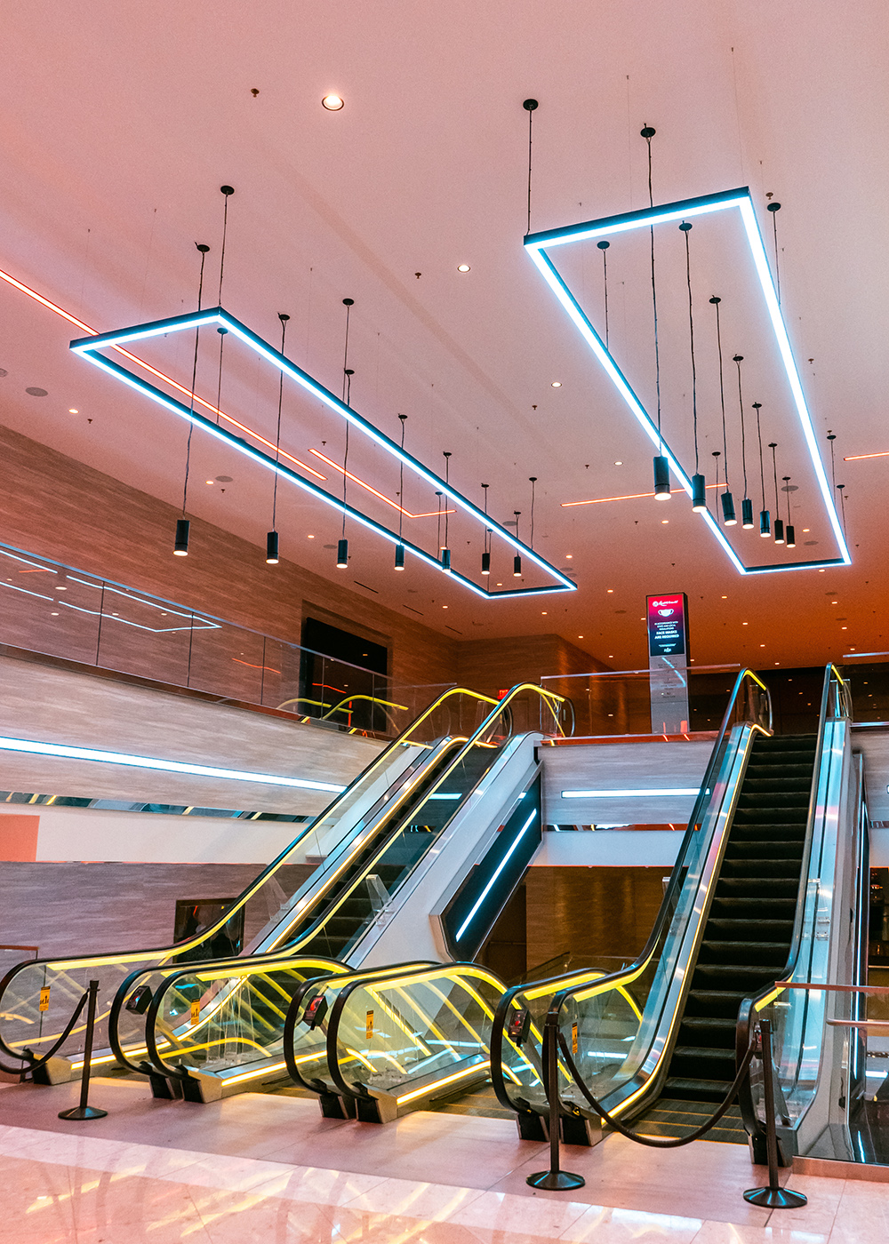 Escalators at Resorts World Las Vegas beneath geometric ceiling lighting and suspended cylinders