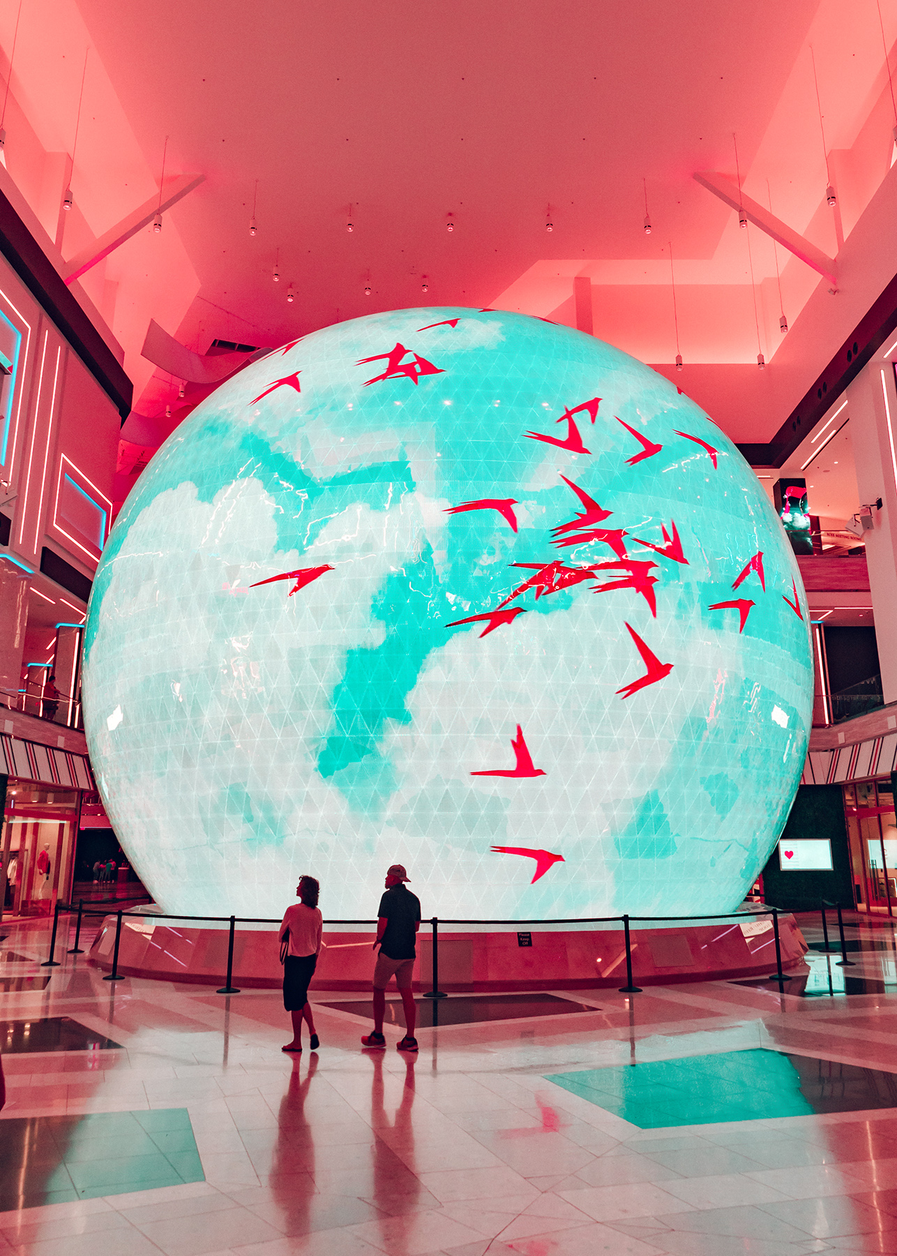 Visitors standing before The Globe displaying animated graphics beneath pink ambient lighting