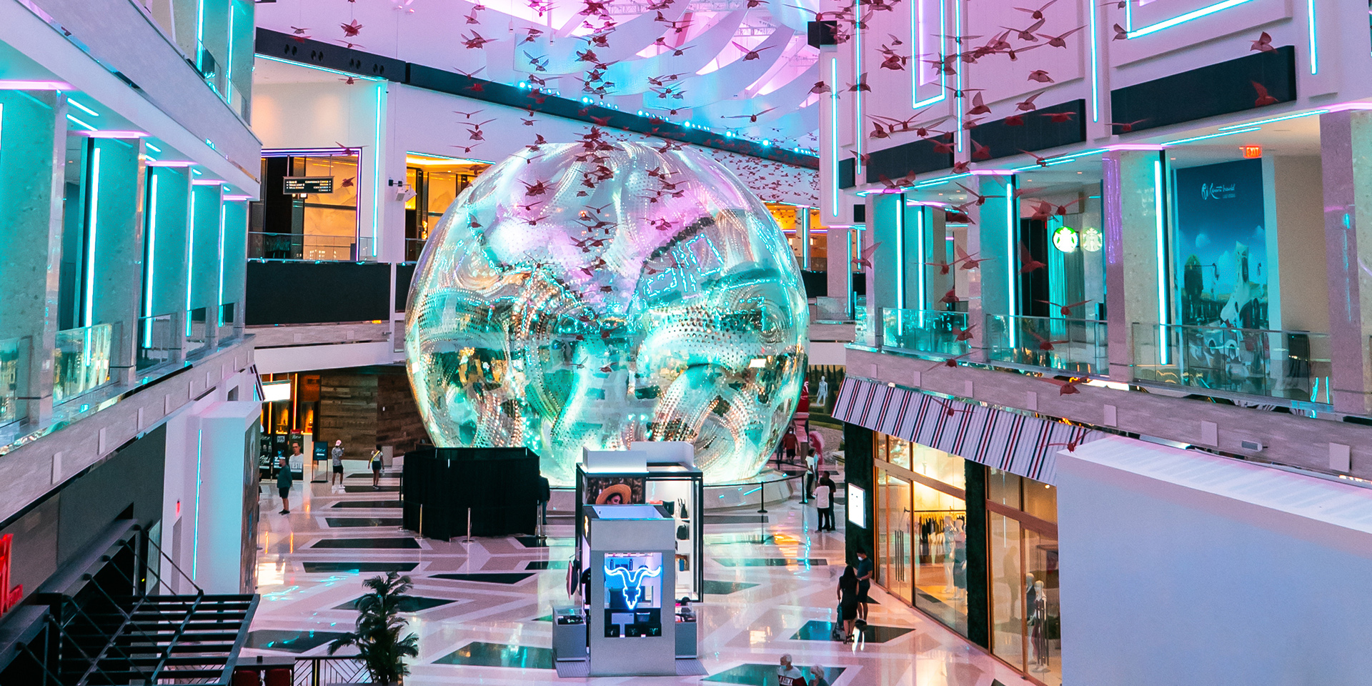 The Globe framed by retail storefronts and turquoise linear lighting in The District at Resorts World Las Vegas